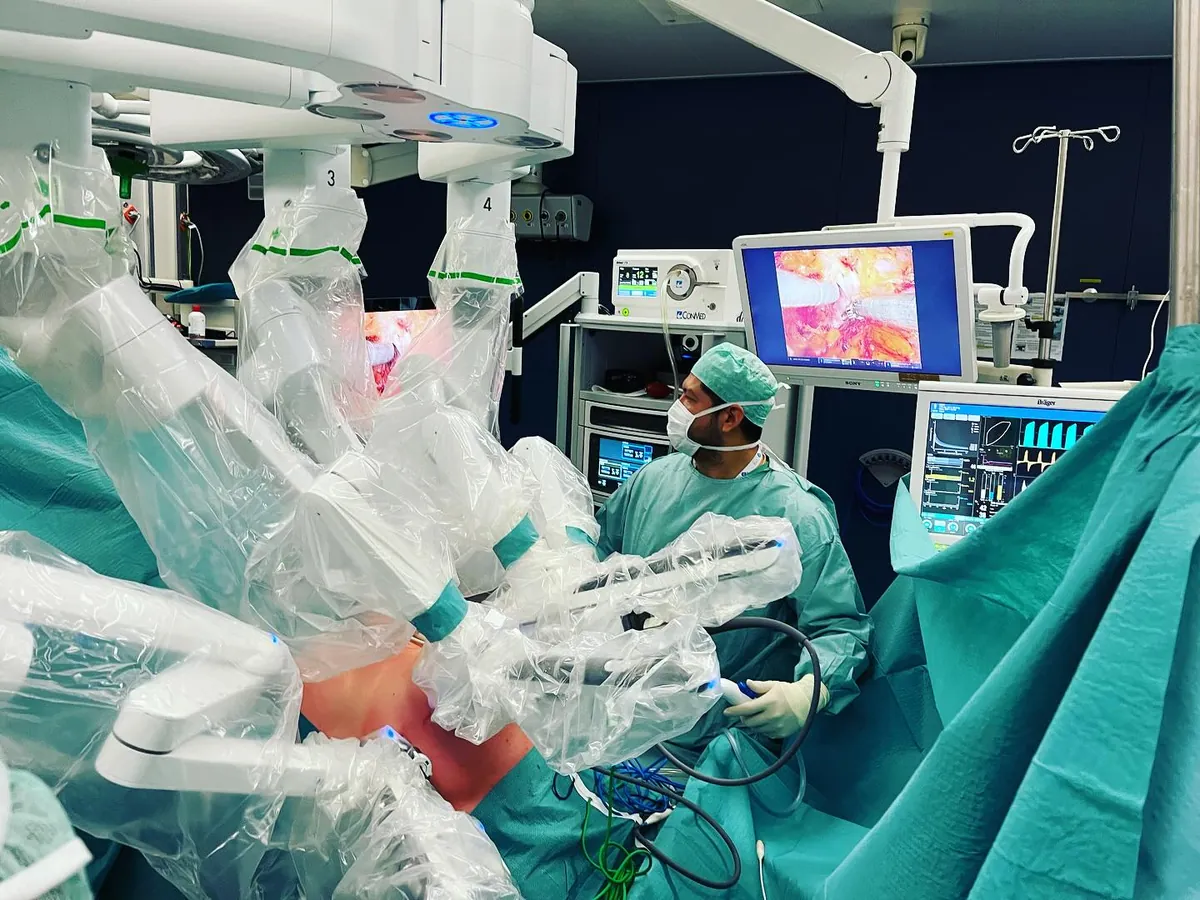 Cirujano en quirófano durante una cirugía robótica, con los brazos del sistema robótico y el monitor con imagen ampliada